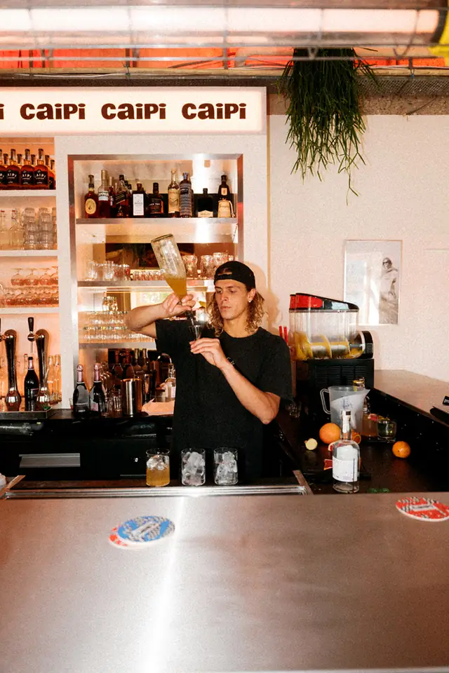 Barman achter de bar van Caipi Café, met de lichtbak met de naam Caipi erboven