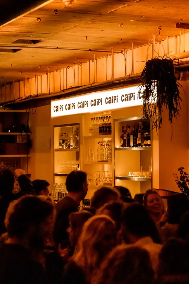 De bar van Caipi Café ’s avonds, vol gasten, met de verlichte Caipi-letters