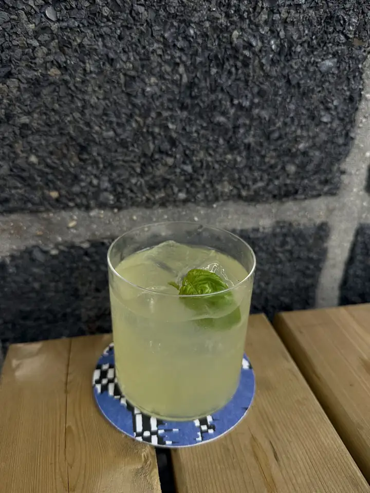 Cocktail met limoen en basilicum op een houten tafel, op een ruitjesonderzetter