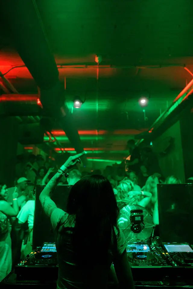 DJ achter de draaitafels in groen licht, met dansende gasten