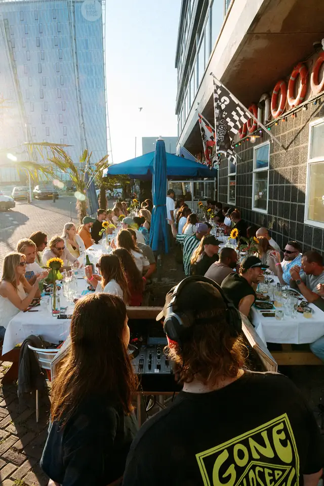 Gasten aan een lange tafel buiten, in de zon aan de haven